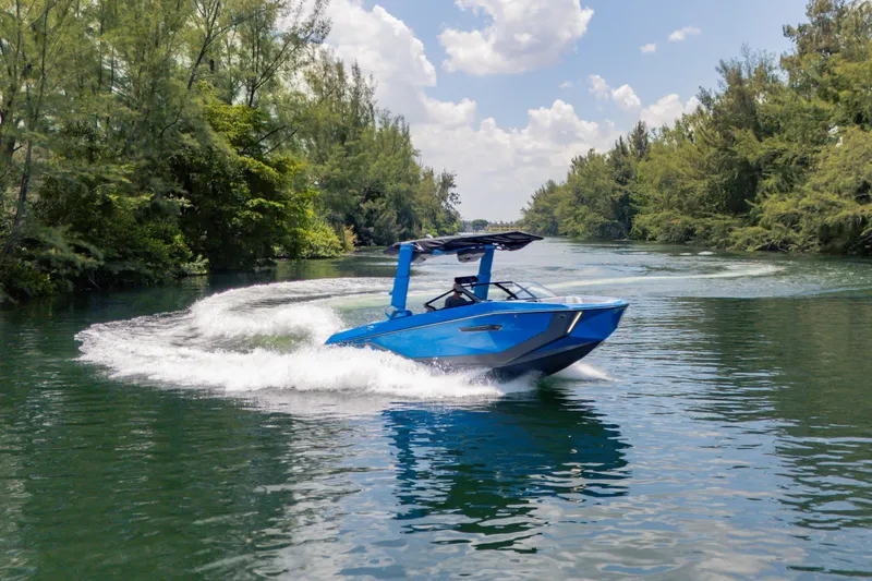  Yacht Photos Pics 2026 Nautique Super Air Nautique G23 cruising on a scenic, tree-lined waterway.