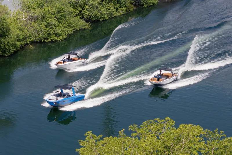  Yacht Photos Pics Three 2026 Nautique Super Air Nautique G23 boats cruising on a scenic waterway.