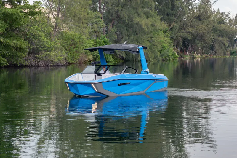  Yacht Photos Pics 2026 Nautique Super Air Nautique G23 boat on a serene lake, surrounded by lush greenery.