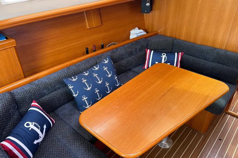 Kokua Yacht Photos Pics 2004 Hunter 33 yacht interior with wooden table, anchor-themed cushions, and cozy seating.