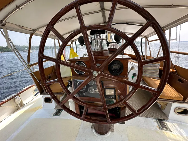 Interlude X Yacht Photos Pics Wooden helm of 1985 Custom Thomas Colvin "Pipistrelle" sailboat, overlooking serene waters.