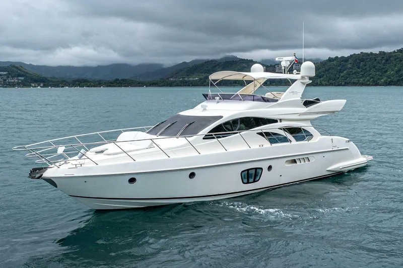 Hakuna Matata Yacht Photos Pics 2007 Azimut 55 yacht cruising on a serene, cloudy sea with lush hills in the background.