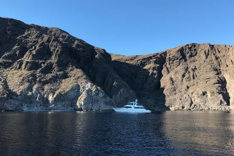 Front Row Yacht Photos Pics 2006 NorthCoast PILOTHOUSE yacht near rugged cliffs under clear blue sky.