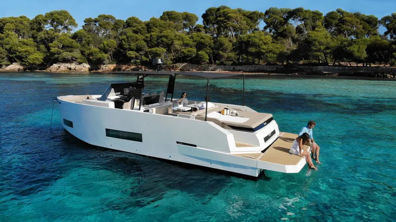  Yacht Photos Pics 2026 De Antonio Yachts D42 cruising in clear blue waters near a lush, tree-lined shore.