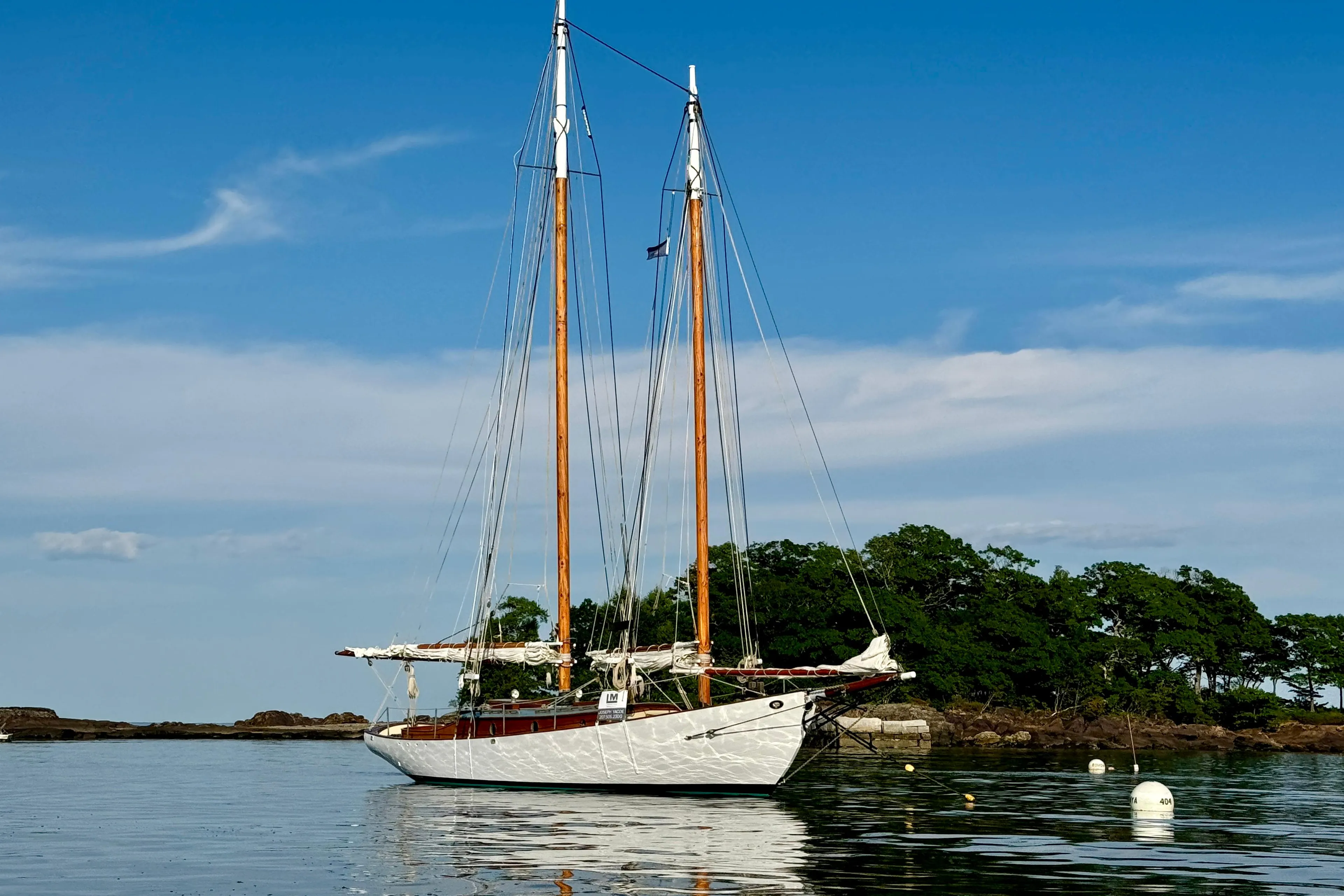 Sailing yacht "John Alden Malabar II" anchored near a lush island, clear blue sky.