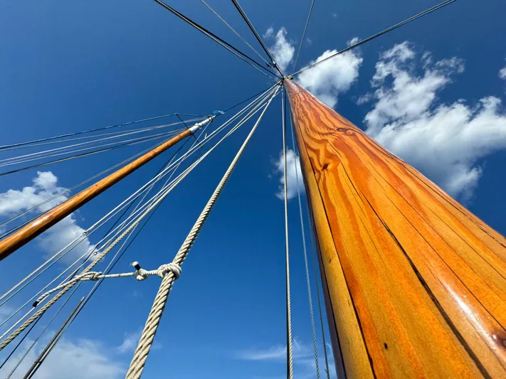 Alyria Yacht Photos Pics Tall wooden mast of John Alden Malabar II sailboat against blue sky, 1996 model.