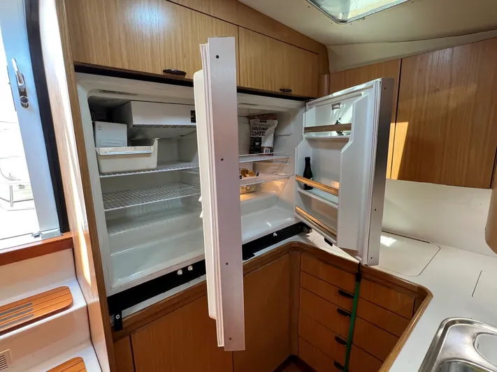 Chaos Yacht Photos Pics 1996 Tiara Yachts 4300 Open kitchen with open refrigerator, wooden cabinets, and countertop.