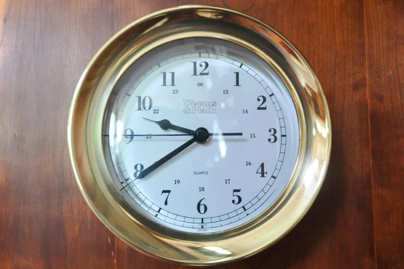 Jezebel Yacht Photos Pics Brass wall clock with white face and black numerals on wooden background.