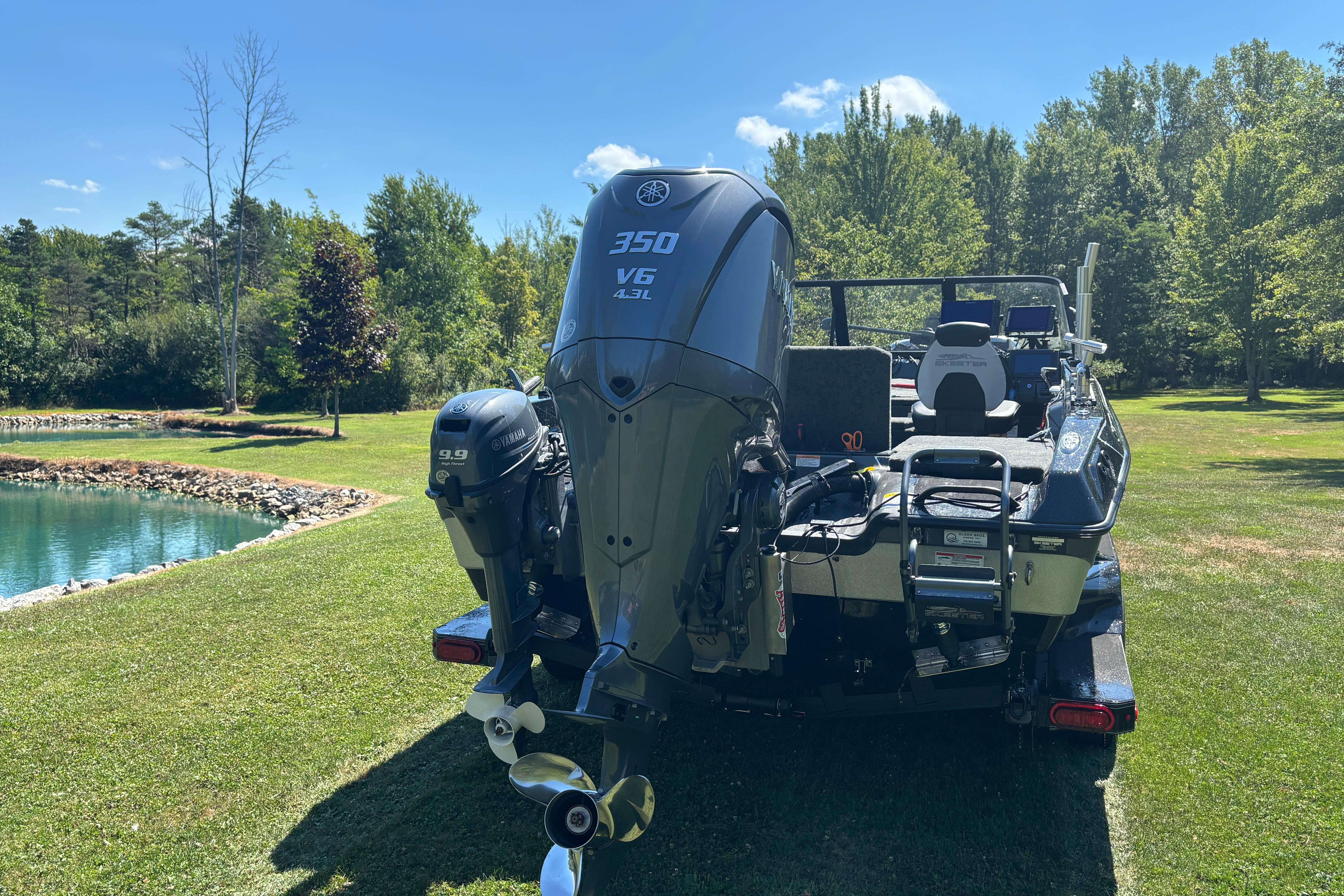 2025 Skeeter WXR2260 boat with powerful outboard motors, parked on grassy area near a pond.