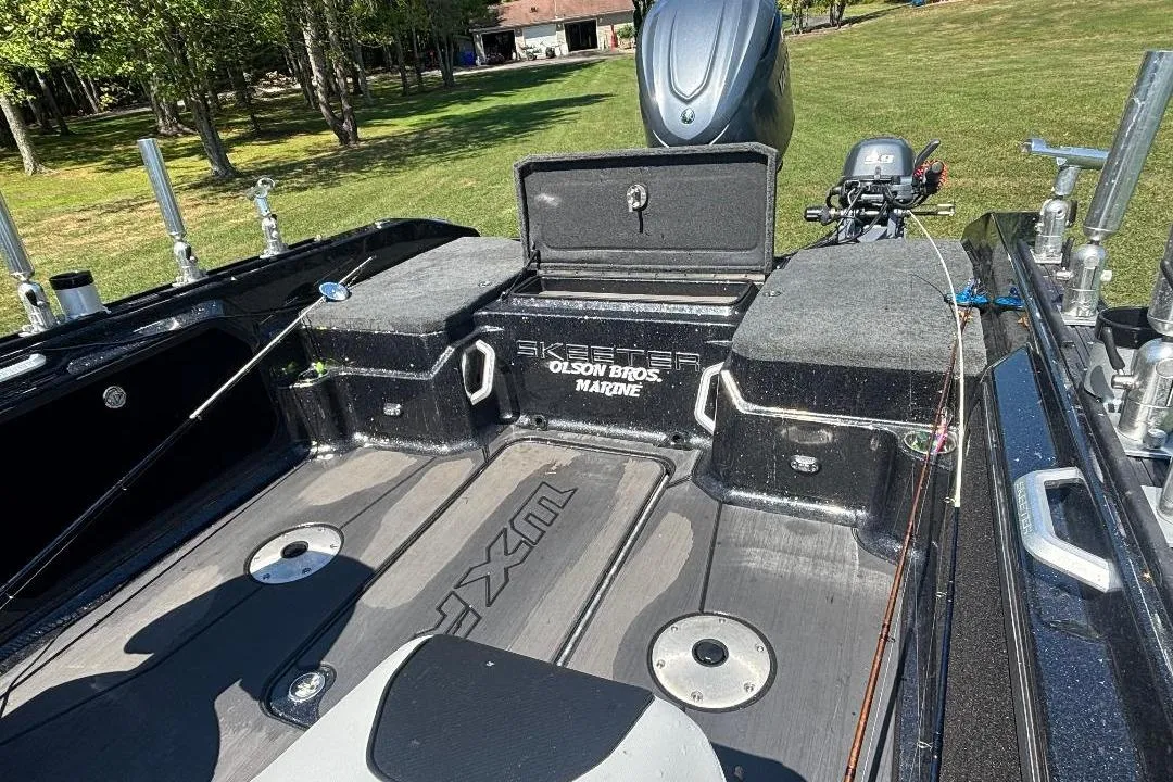 2025 Skeeter WXR2260 boat interior with fishing gear, open storage, and motor in a grassy area.
