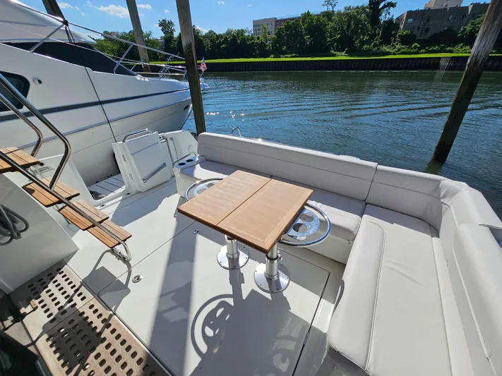  Yacht Photos Pics 2024 Beneteau Antares 12 yacht deck with seating and table, docked by a serene river.