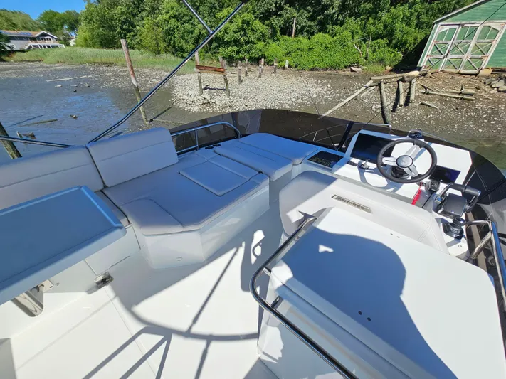  Yacht Photos Pics 2024 Beneteau Antares 12 boat interior with steering wheel and seating, docked near a shoreline.
