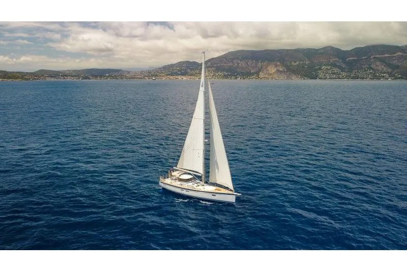  Yacht Photos Pics 2023 Hallberg-Rassy 50 sailing yacht on open sea with mountainous coastline in background.