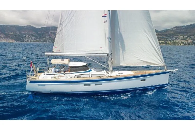  Yacht Photos Pics 2023 Hallberg-Rassy 50 sailing yacht on open sea with mountains in background.