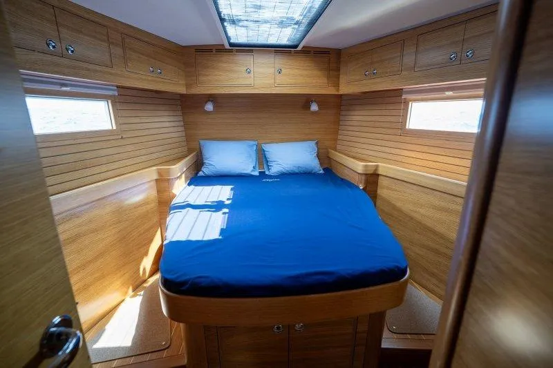  Yacht Photos Pics Luxurious 2023 Hallberg-Rassy 50 yacht cabin with wooden interior and blue bedding.