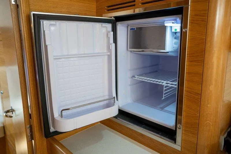  Yacht Photos Pics 2023 Hallberg-Rassy 50 yacht interior fridge, open with wooden cabinetry.