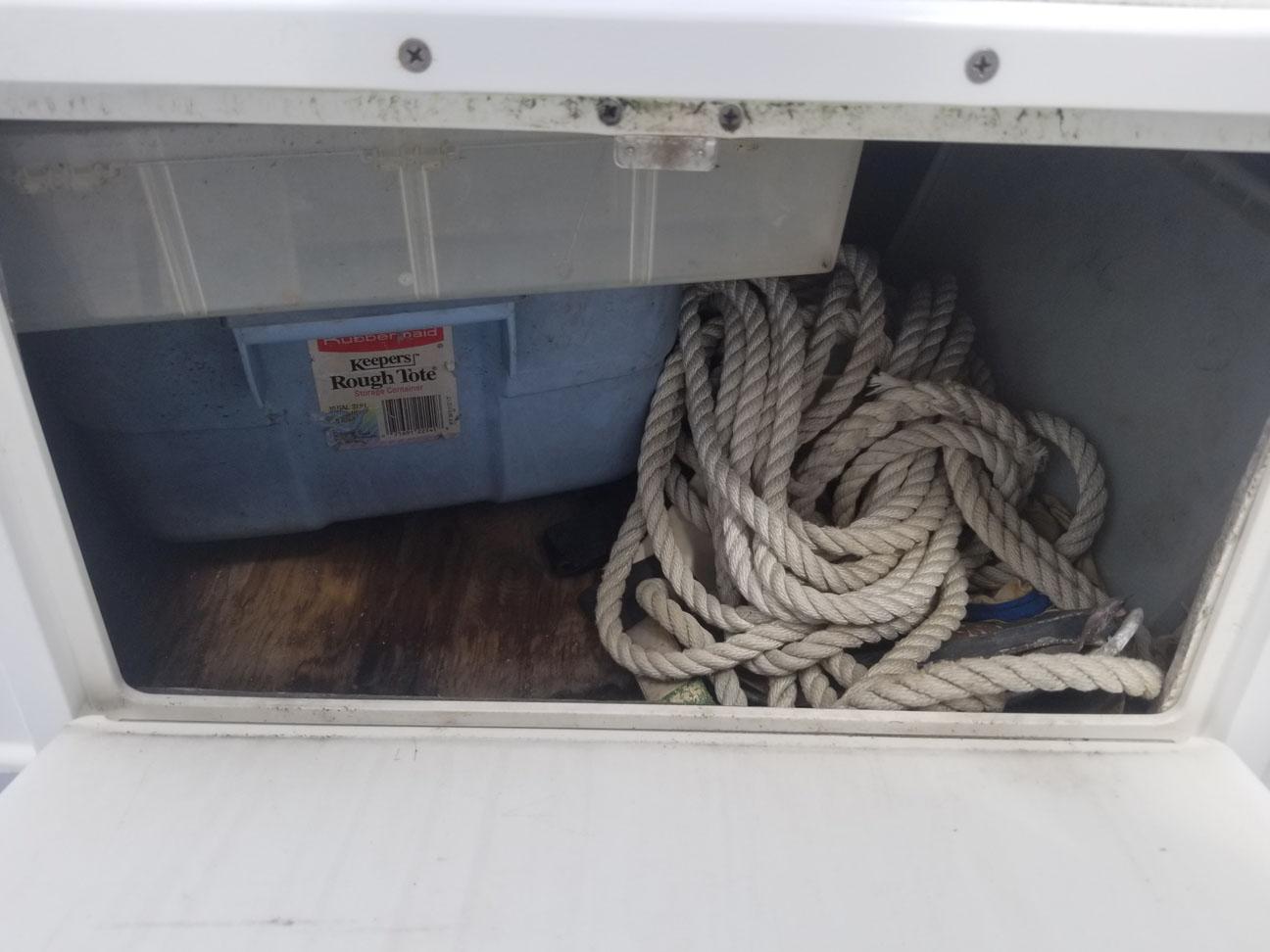 Storage compartment with coiled rope and blue container on a 1977 Pace Wahoo boat.