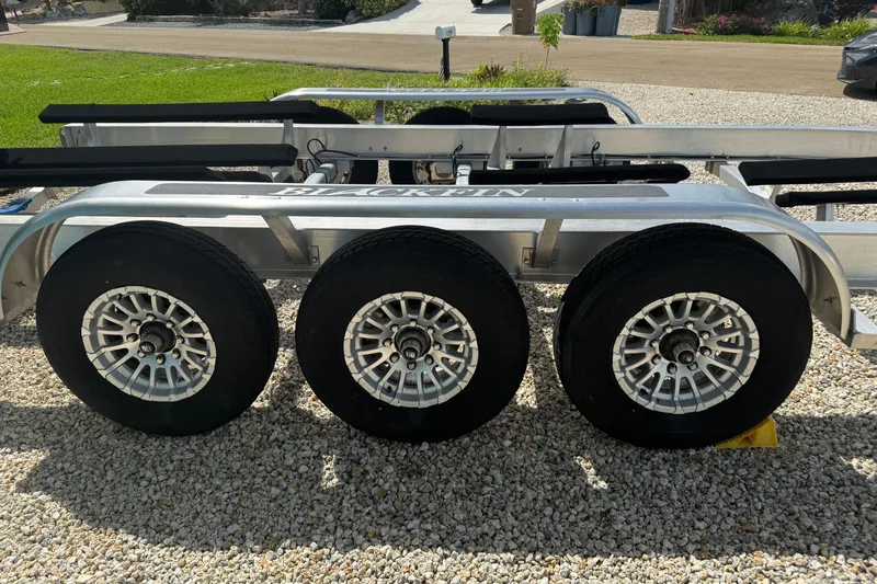  Yacht Photos Pics Triple-axle trailer for 2024 Blackfin 332 CC boat on gravel surface.