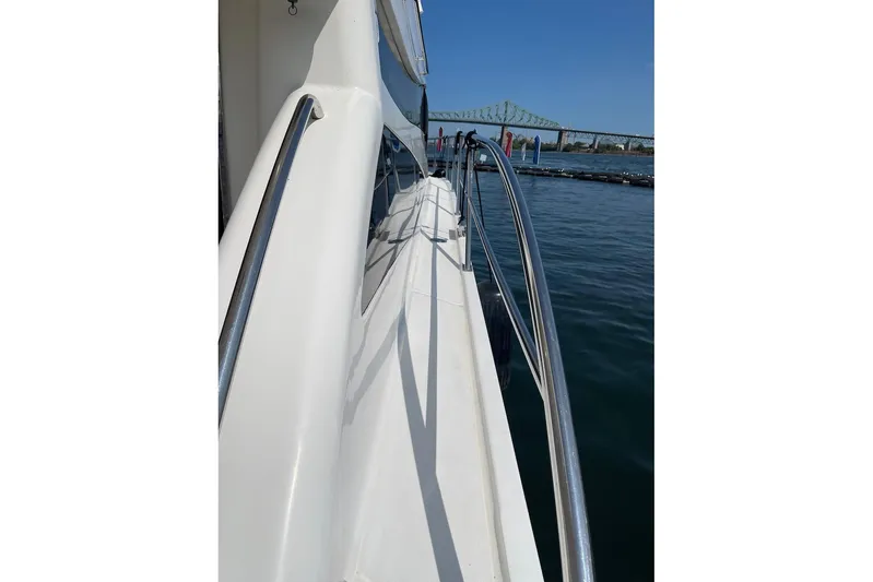 Passe Ports V Yacht Photos Pics 2004 Neptunus 56 Flybridge yacht with sleek railing, docked near a bridge.