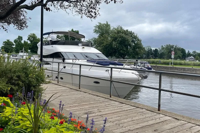Passe Ports V Yacht Photos Pics 2004 Neptunus 56 Flybridge yacht docked by a wooden walkway, surrounded by vibrant flowers.