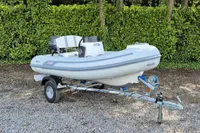 2022 AB Inflatables 9.5 Alx boat on trailer, parked on gravel with green foliage background.