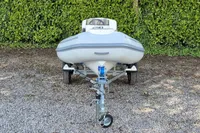 2022 AB Inflatables 9.5 Alx boat on trailer, parked on gravel with green foliage background.