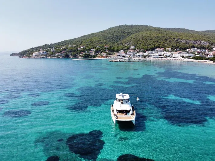 Yacht Photos Pics 2020 Leopard 43 Powercat anchored in clear turquoise waters near a coastal village.