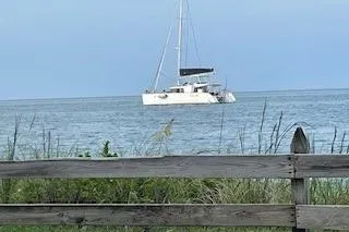  Yacht Photos Pics 2019 Lagoon 450 catamaran sailing on calm sea, viewed from behind a wooden fence.