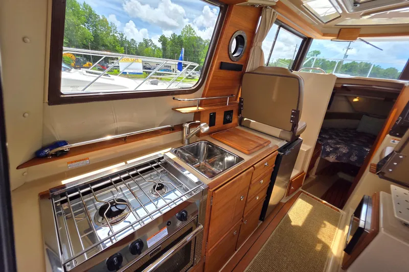 Seamore Yacht Photos Pics 2020 Ranger Tugs R27LE interior kitchen with stove, sink, and wooden cabinetry.