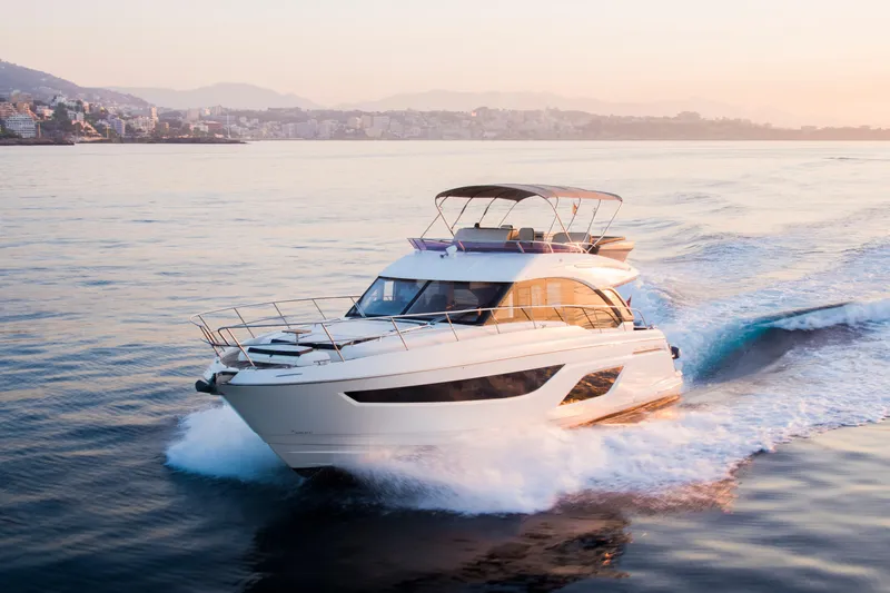 Valluga Yacht Photos Pics Luxurious 2018 Bavaria R55 yacht cruising at sunset near coastal cityscape.