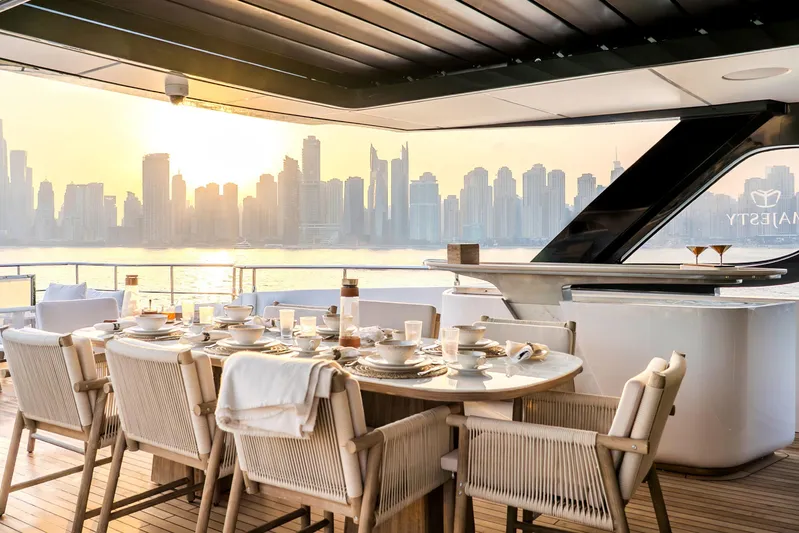  Yacht Photos Pics Luxury dining setup on Majesty 100 Terrace yacht, 2027, with city skyline at sunset.