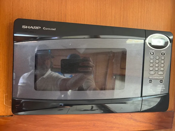  Yacht Photos Pics Sharp Carousel microwave oven mounted on a wooden cabinet, reflecting surroundings.