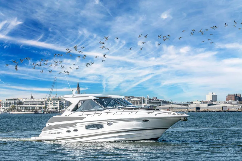  Yacht Photos Pics 2016 Regal 46 Sport Coupe cruising on water with cityscape and birds in the background.