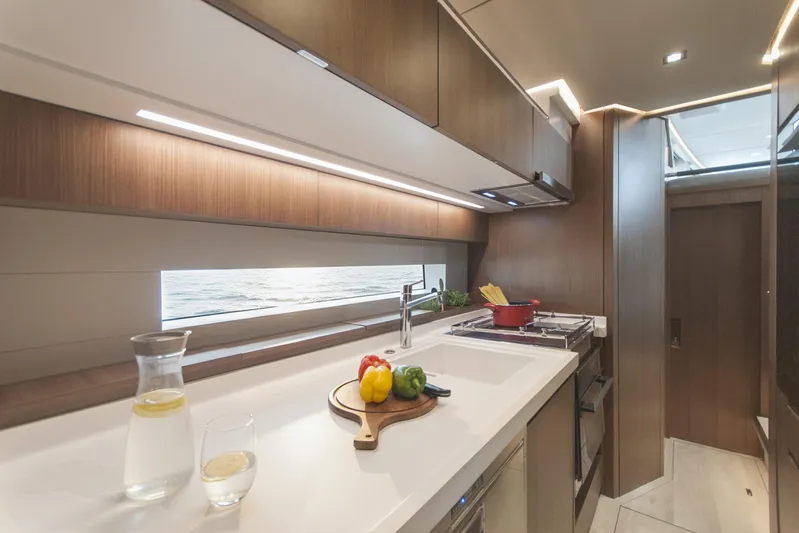 Savoir Faire Yacht Photos Pics Modern yacht kitchen interior with sleek wood cabinetry, featuring a countertop and ocean view window.