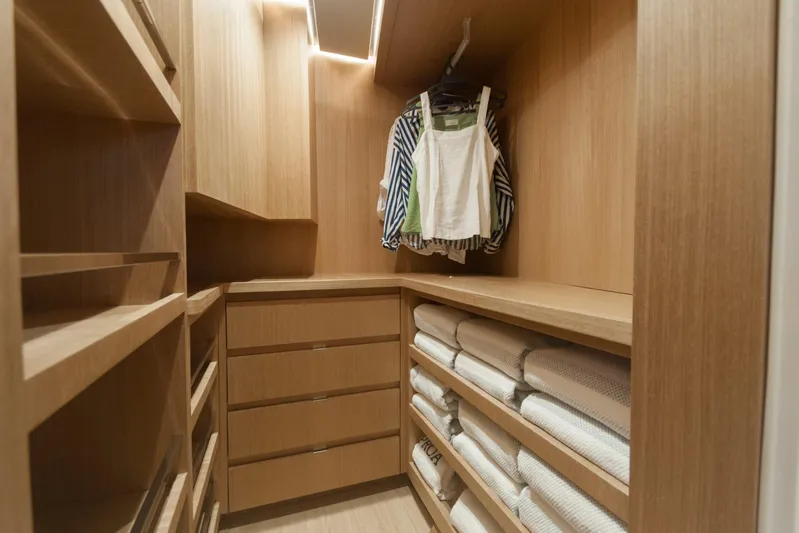 Savoir Faire Yacht Photos Pics Modern wooden closet with shelves and drawers, featuring neatly folded towels and hanging clothes.