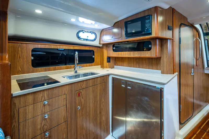 Bottoms Up II Yacht Photos Pics 2009 Pursuit OS 375 Offshore yacht kitchen with wood cabinetry, sink, stove, and microwave.