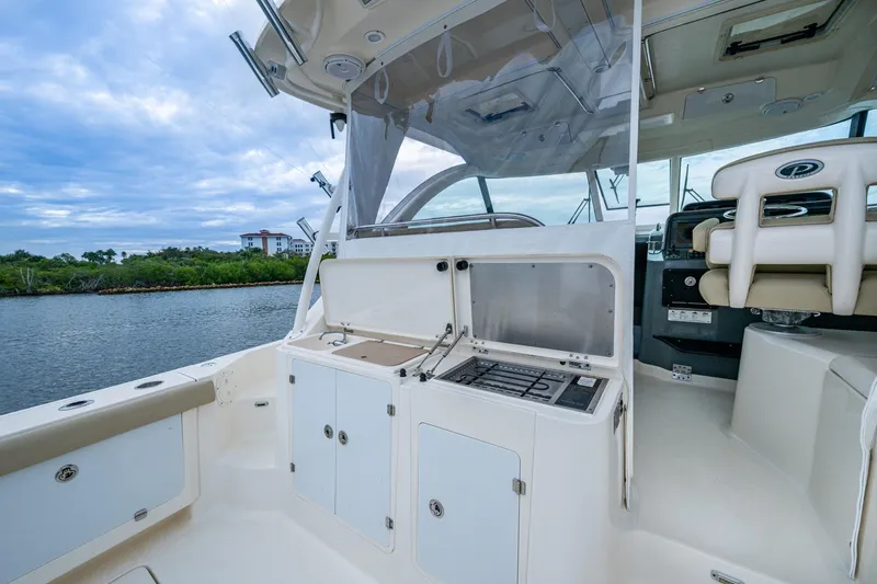 Bottoms Up II Yacht Photos Pics 2009 Pursuit OS 375 Offshore boat interior with helm and seating, docked by lush greenery.
