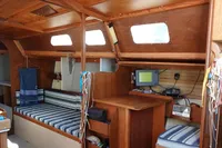 Cozy wooden boat interior with striped seating, navigation equipment, and natural light from windows.