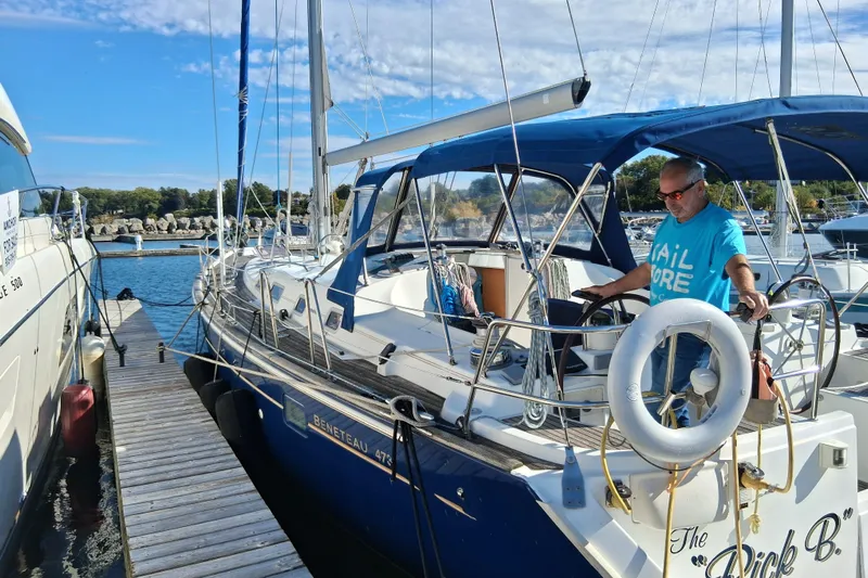 Rick B Yacht Photos Pics Man steering a 2006 Beneteau 473 sailboat docked at a marina.