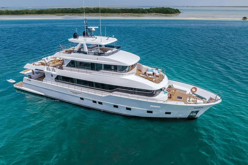  Yacht Photos Pics Luxurious 2026 Nomad 101 yacht cruising in clear blue waters near a sandy shoreline.