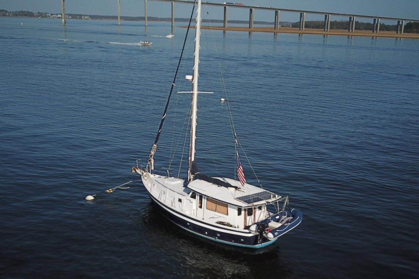 1979 Schucker 436 Motorsailor anchored on calm water near a bridge.