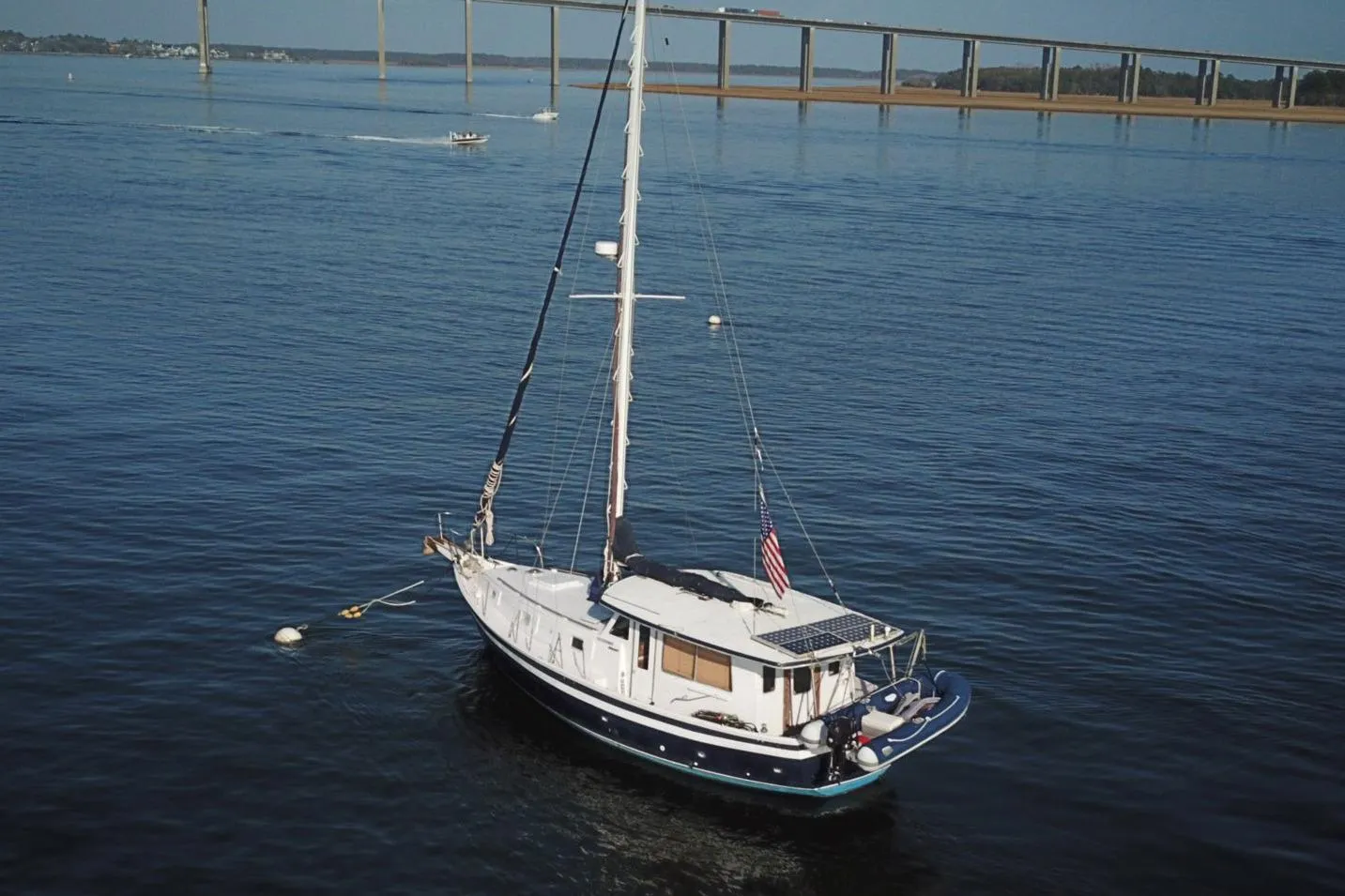 1979 Schucker 436 Motorsailor anchored on calm water near a bridge.