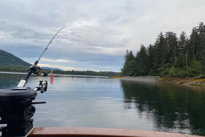 Points North III Yacht Photos Pics Fishing rod on Kadey-Krogen 42 boat, serene lake, forested shoreline, overcast sky, 1986 model.