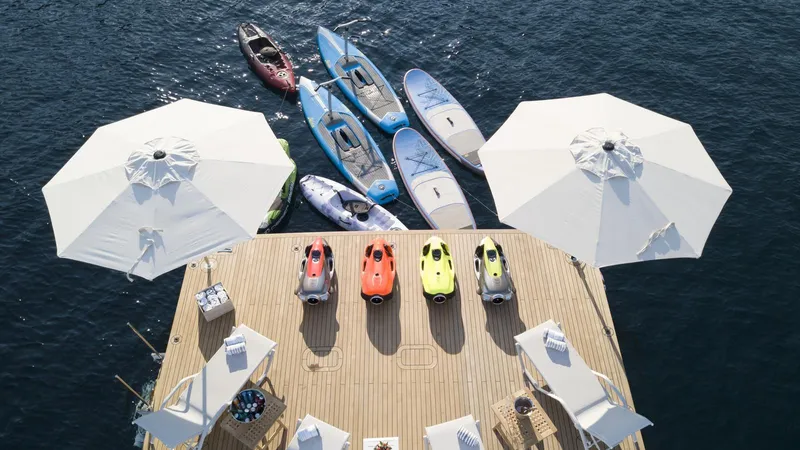 All About U Yacht Photos Pics 2018 Ada Yacht deck with kayaks, paddleboards, and umbrellas on calm water.