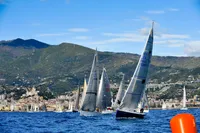Sailboats racing near a coastal town with mountains, featuring a 1997 Custom IMS proto 33'.