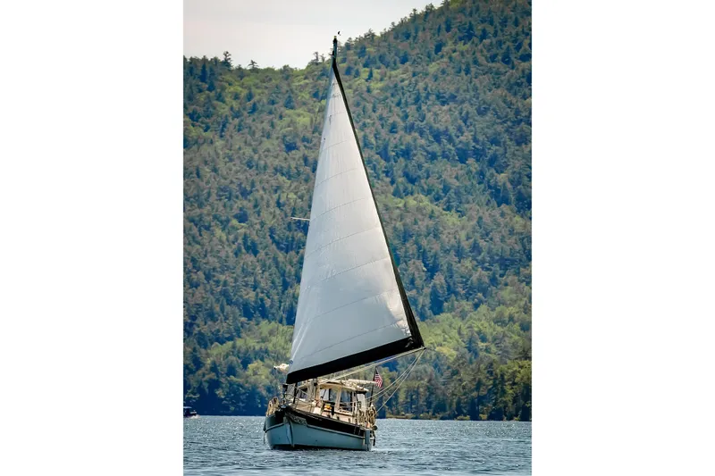 Rhythm Yacht Photos Pics Sailboat Gozzard 31 (1991) gliding on water with forested hills in background.