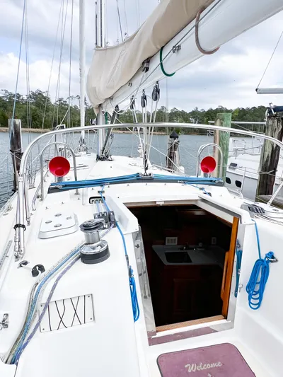 Alacrity Yacht Photos Pics 1998 Saga 43 sailboat deck with open cabin entrance, docked by a serene waterfront.