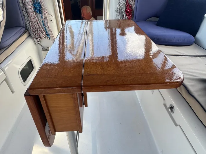Sanctuary Yacht Photos Pics Polished wooden table on 2005 Beneteau Oceanis Clipper 473 yacht, with cushioned seating and nautical ropes.