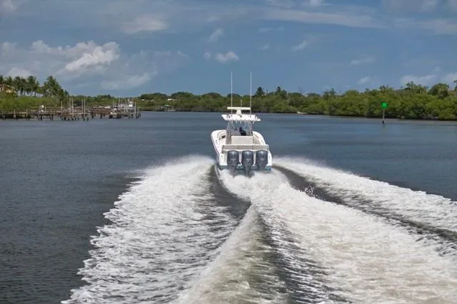  Yacht Photos Pics Invincible 36 boat cruising on a river, leaving a wake, under a clear blue sky.