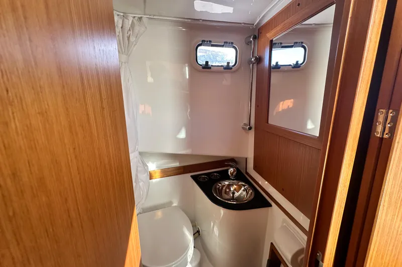  Yacht Photos Pics 2025 Sargo 31OB boat bathroom with wooden accents, compact sink, and porthole windows.